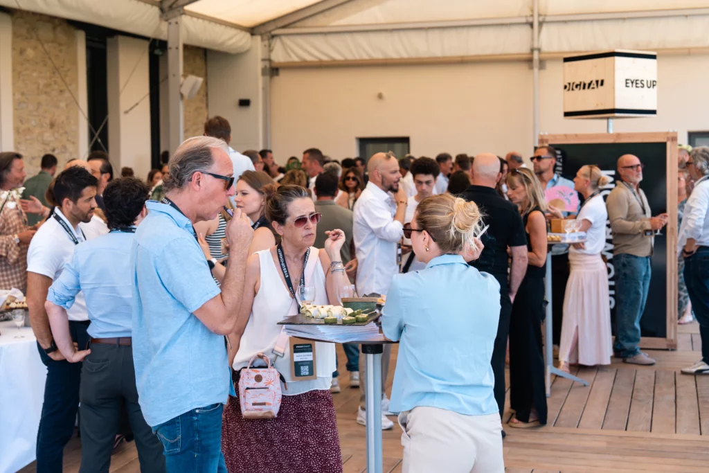 Crowded indoor networking event with people chatting, sampling appetizers, and standing around food tables.