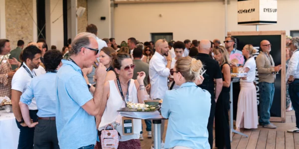 Crowded indoor networking event with people chatting, sampling appetizers, and standing around food tables.