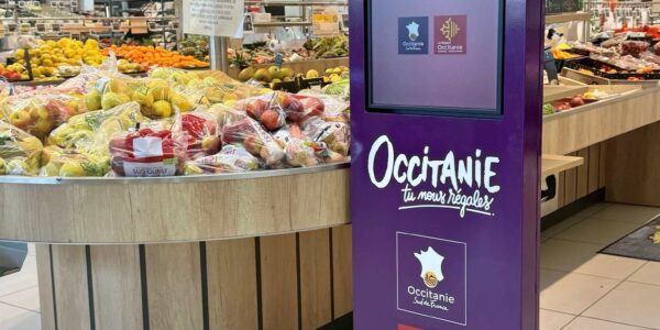 Purple promotional kiosk in a supermarket for Occitanie, surrounded by fruit display and produce sections.