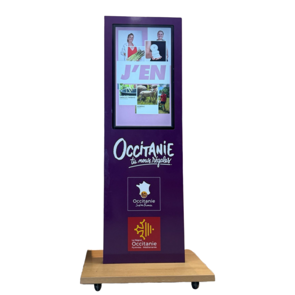 Tall purple display panel on a wooden platform with a photo collage and a large J'EN sign, featuring Occitanie logos and regional imagery against a black backdrop.